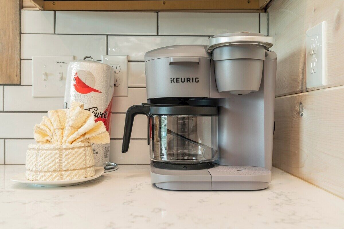 Eine Kaffeemaschine von Keurig auf einer Küchenarbeitsplatte, mit einem Einweg-Kaffeepad und einer Kaffeetasse.