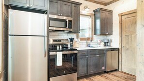 A modern kitchen with stainless steel appliances, dark wooden cabinets, and a wooden floor.