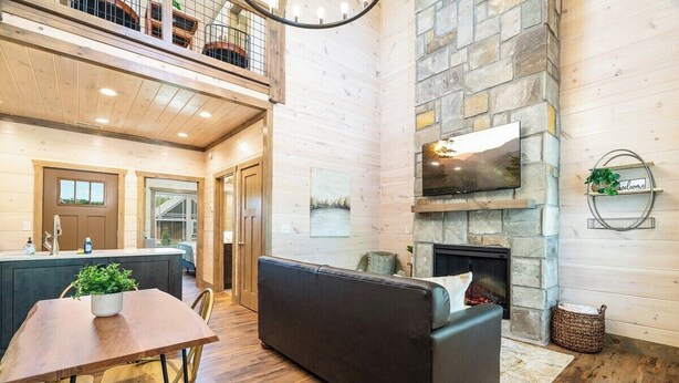 A spacious living area with a stone fireplace, a black sofa, and a dining table with chairs. - 5 Minutes From Dollywood/In DwTn Pigeon Forge (Pigeon Forge)
