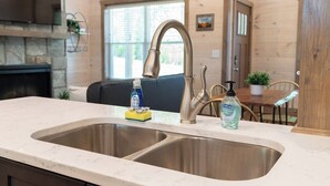 A kitchen with a double stainless steel sink, a stone fireplace, and a dining area with a wooden table and chairs. - 5 Minutes From Dollywood/In DwTn Pigeon Forge (Pigeon Forge)