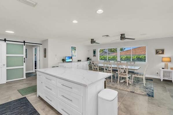 Een moderne keuken met een groot eiland, een eethoek met tafel en stoelen, en uitzicht op buiten.