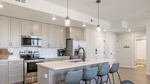 A modern kitchen with stainless steel appliances, a large island with bar stools, and pendant lighting.