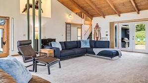 A spacious living room with a large sectional sofa, a leather armchair, and a small wooden table. A staircase with a wooden railing leads to an upper level. - The Bodega House~Bodega Bay~Near Beach~Family Fun~Game Room~Sonoma Coast Fun! (Bodega Bay)