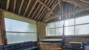 A rustic interior with a stone wall, wooden ceiling beams, a round table, and a sofa. - Propriété au Calme Avec Piscine au Coeur de L'anjou ! Idéale Pour les Familles (Baugé en Anjou)