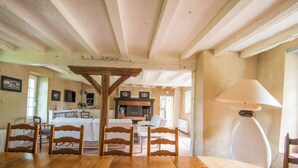 A dining area with a wooden table and chairs, a kitchen in the background, and a lamp on the right. - Propriété au Calme Avec Piscine au Coeur de L'anjou ! Idéale Pour les Familles (Baugé en Anjou)