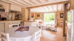 A modern kitchen with white cabinetry, a stainless steel stove, and a dining area with a table and chairs. - Propriété au Calme Avec Piscine au Coeur de L'anjou ! Idéale Pour les Familles (Baugé en Anjou)