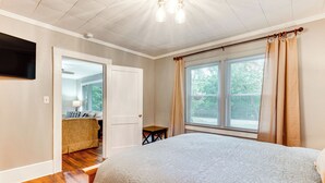 A bedroom with a large bed, a small table, a TV mounted on the wall, and a door leading to another room. - 3 Mi to Dtwn! Forest City Haven w/ Furnished Patio (Forest City)