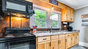 A kitchen with a black stove, wooden cabinets, a granite countertop, a window with a view of trees, and a sign that says "FRESH EGGS". - 3 Mi to Dtwn! Forest City Haven w/ Furnished Patio (Forest City)