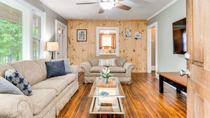 A living room with two sofas, a coffee table, wooden walls, a ceiling fan, and a door. - 3 Mi to Dtwn! Forest City Haven w/ Furnished Patio (Forest City)