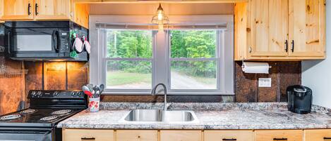 A kitchen with wooden cabinets, a stainless steel sink, a stove, a microwave, and a coffee maker.