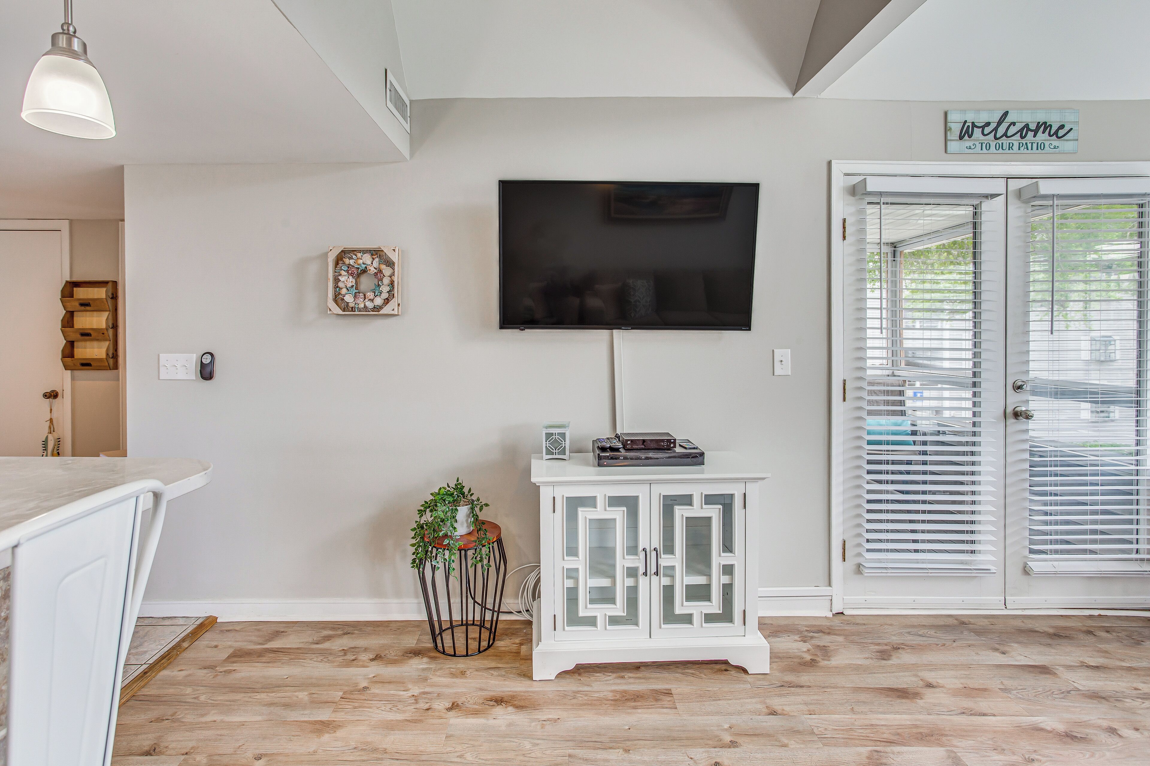 Un salon moderne avec un téléviseur à écran plat fixé au mur, un meuble blanc aux portes en verre et un plancher en bois.