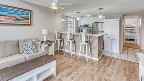 A modern kitchen with white cabinets, a central island with bar stools, a dining area with a wooden table, and a ceiling fan. - 1 Block to Beach: Myrtle Beach Condo w/ Pool! (Myrtle Beach)