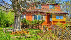 A two-story house with a red and yellow exterior, surrounded by a garden with various plants and a large tree. - Spacious Duluth Home ~ 4 Mi to Lake Superior! (Duluth)