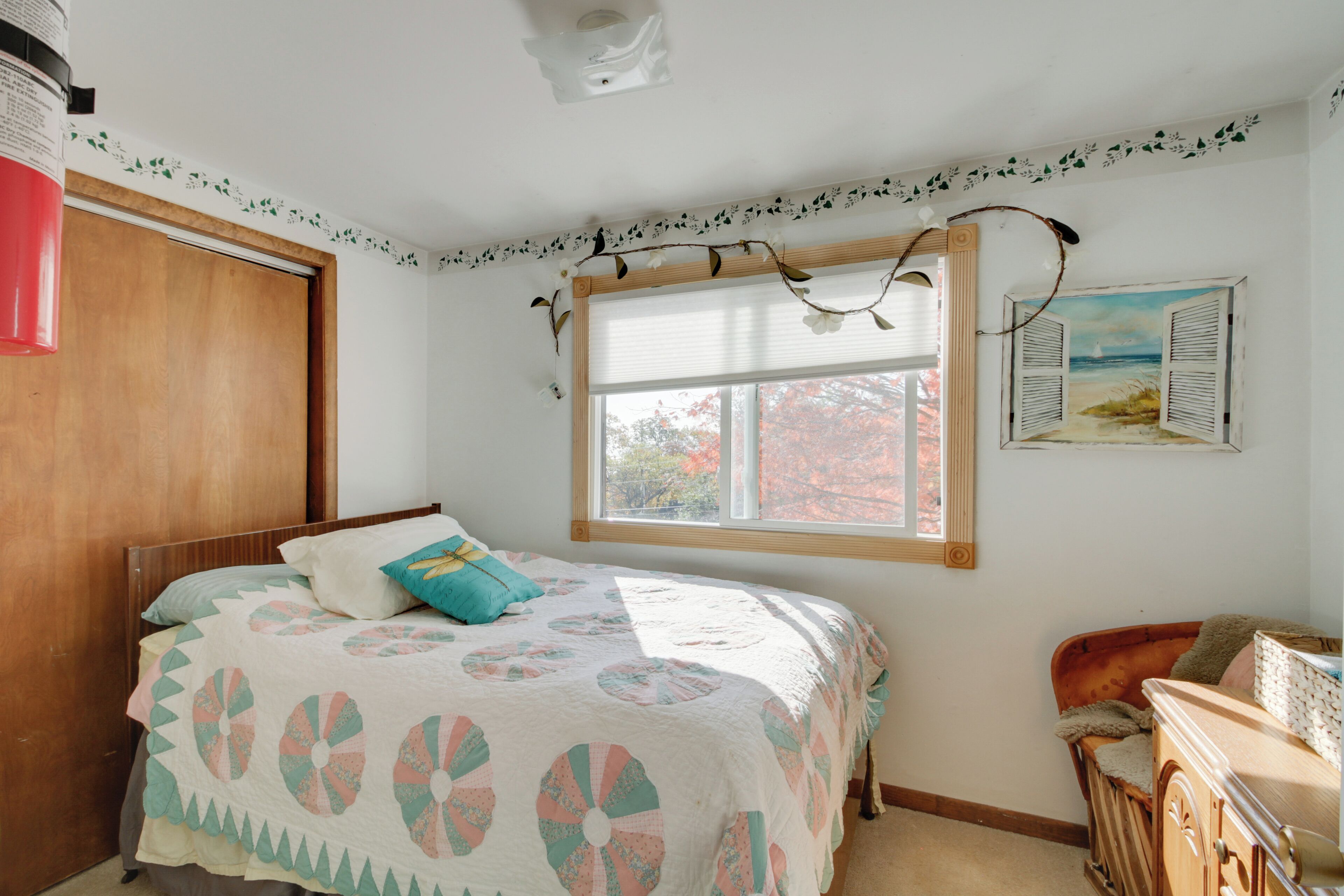 A bedroom with a bed, a window with a view, a wooden wardrobe, and a dresser.