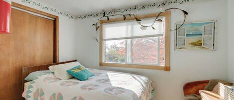 A bedroom with a bed, a window with a view, a wooden wardrobe, and a dresser.