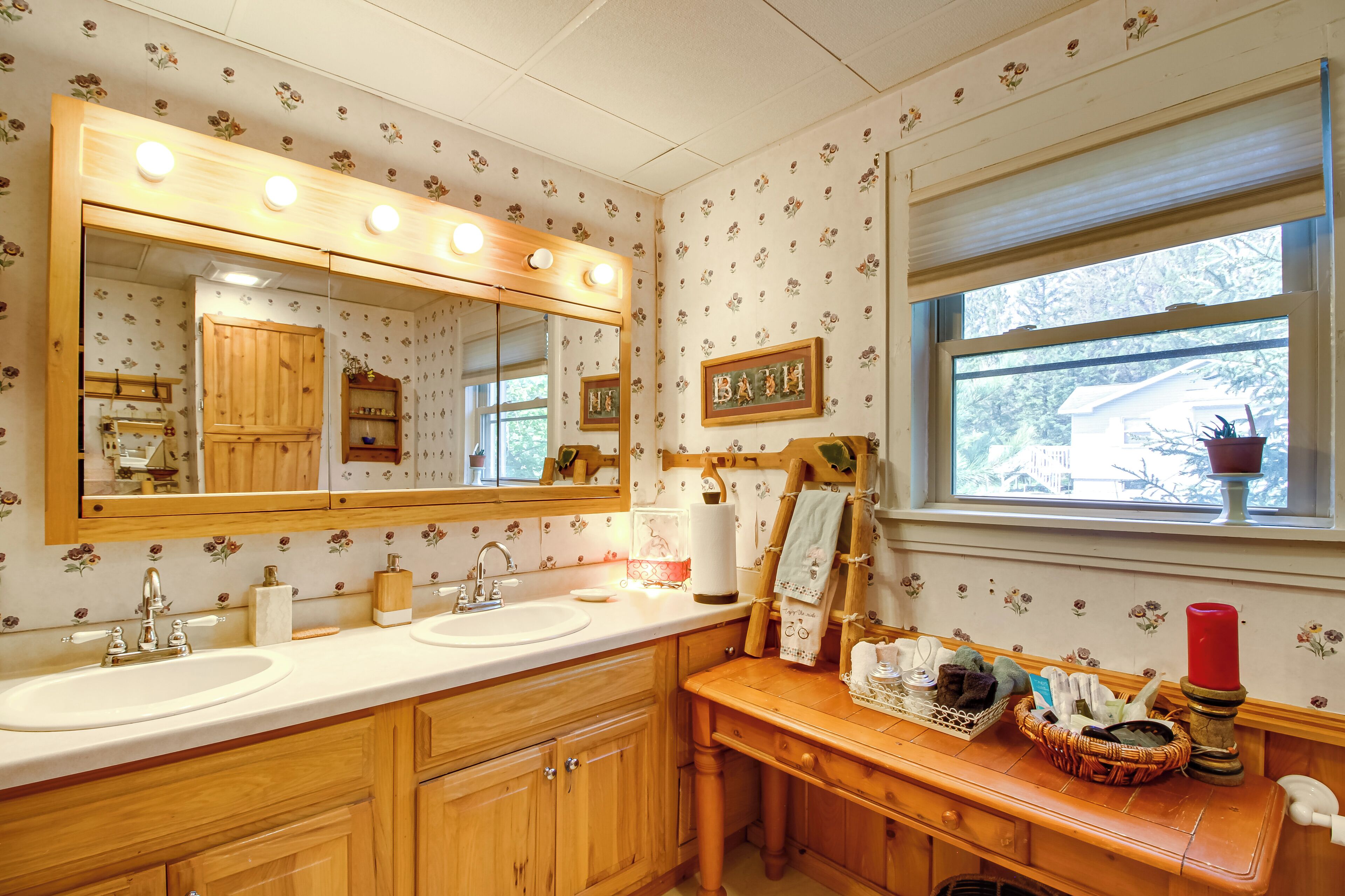 A bathroom with two sinks, a vanity with a mirror, and a window with a view of a house.