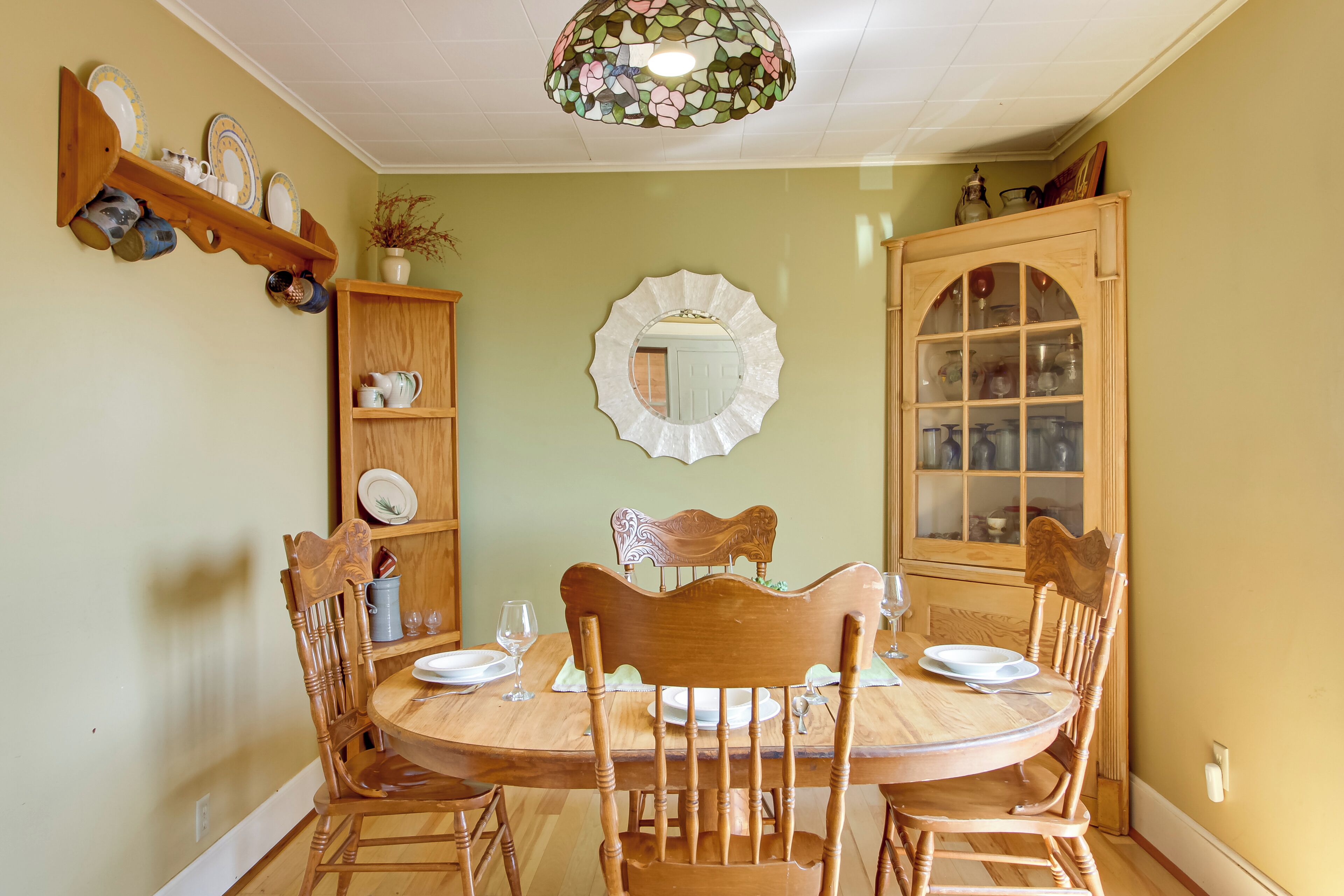 Een eetkamer met een houten tafel, stoelen, een kroonluchter en een spiegel aan de muur.