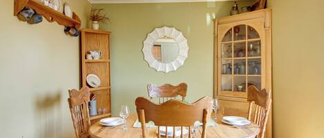 Een eetkamer met een houten tafel, stoelen, een kroonluchter en een spiegel aan de muur.