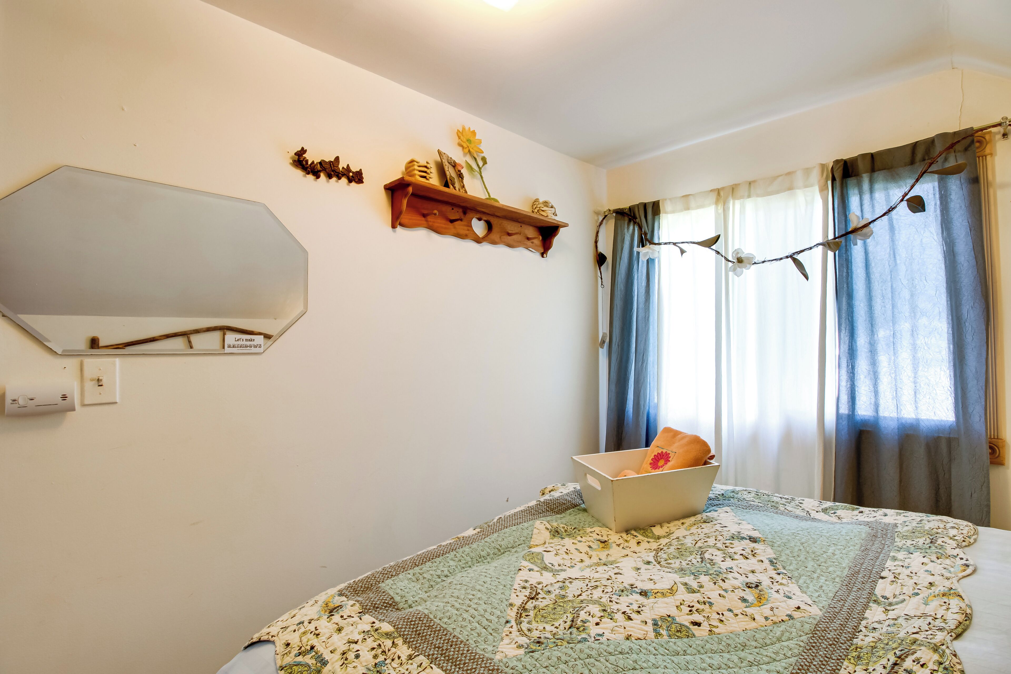 A bedroom with a bed, a dresser, a mirror, a shelf with decorative items, and a window with curtains.