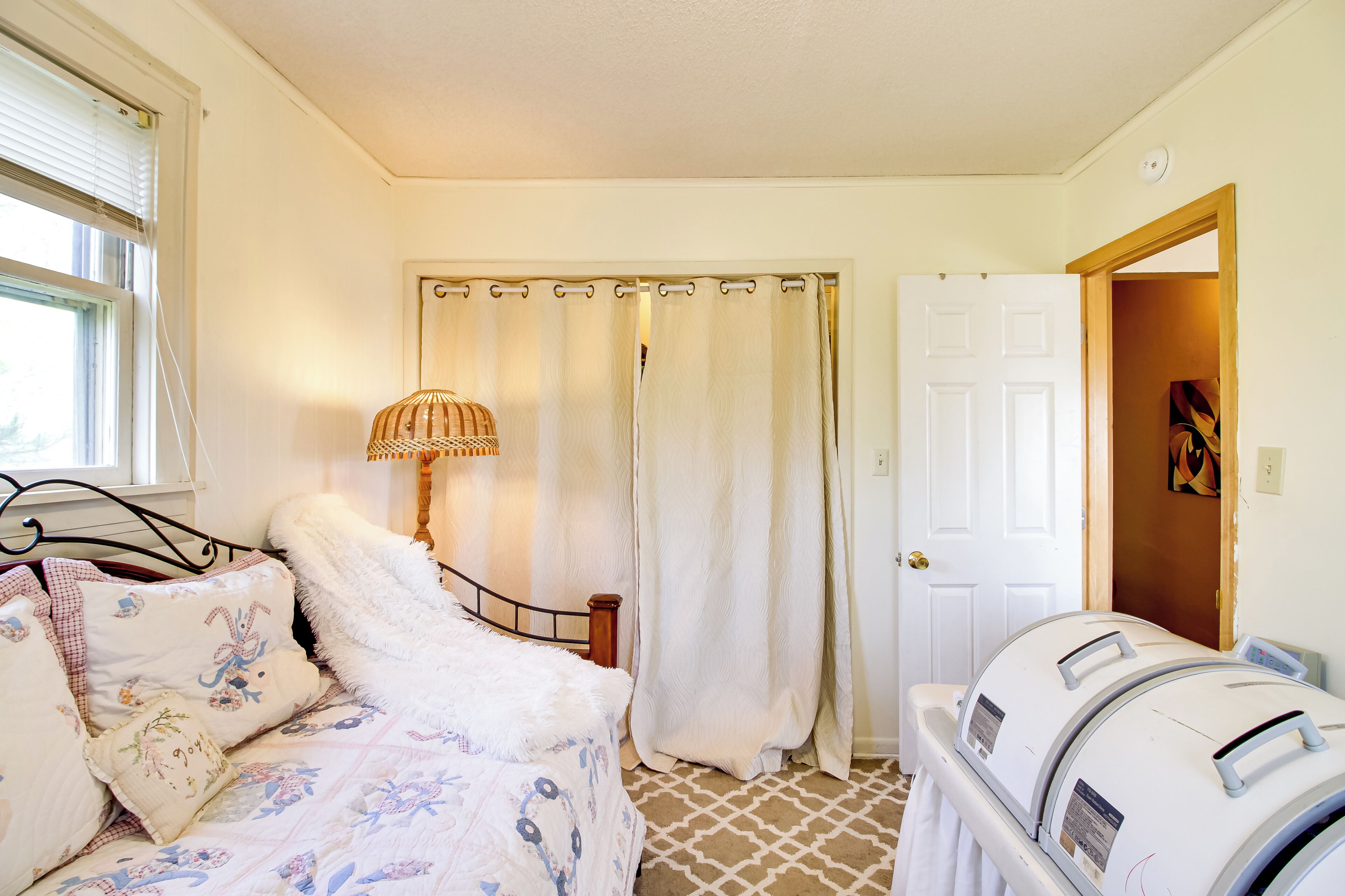 A bedroom with a bed, a lamp, a shower curtain, and a washing machine.