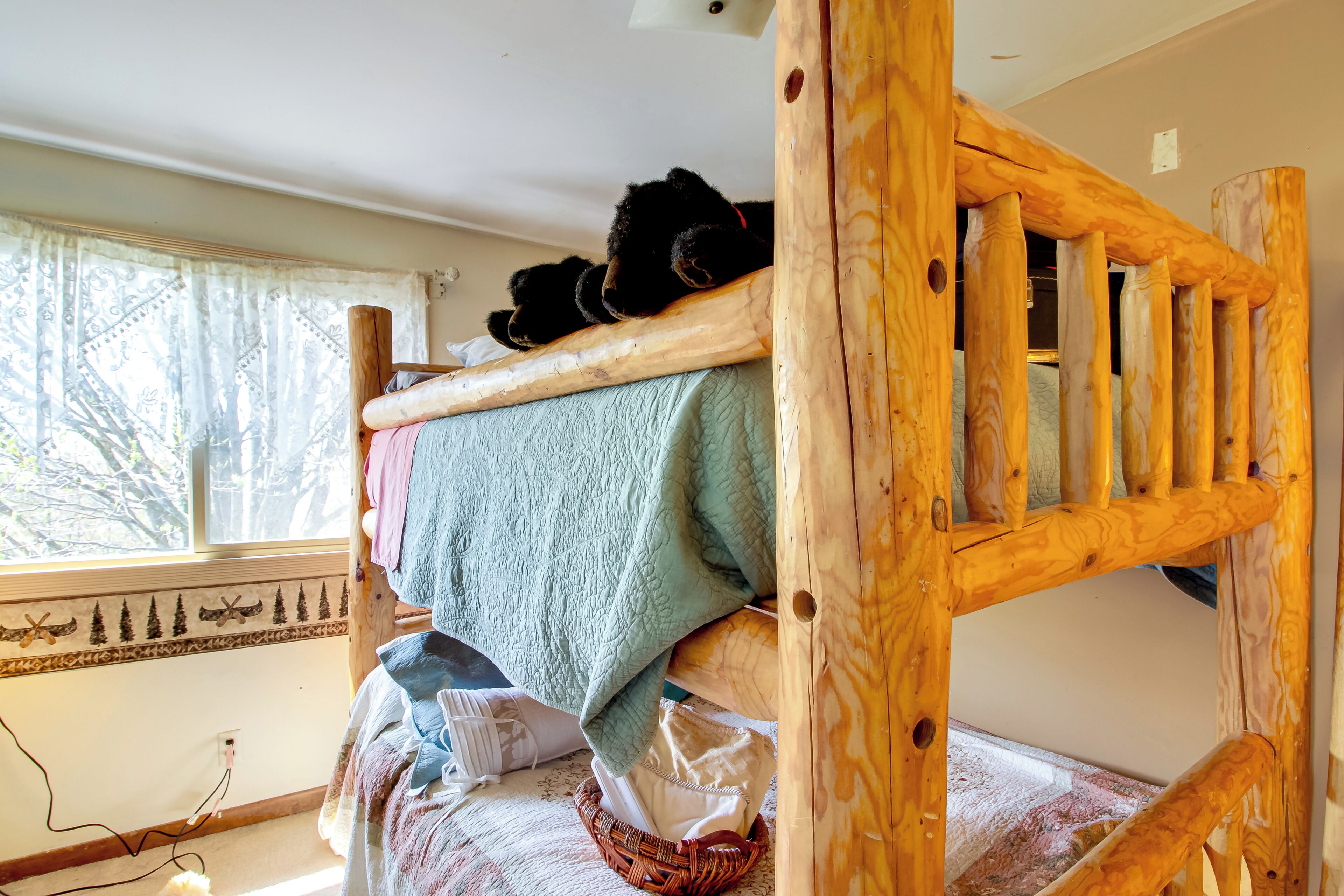 A bunk bed with a wooden headboard, a window with a view of trees, and a patterned wall border.
