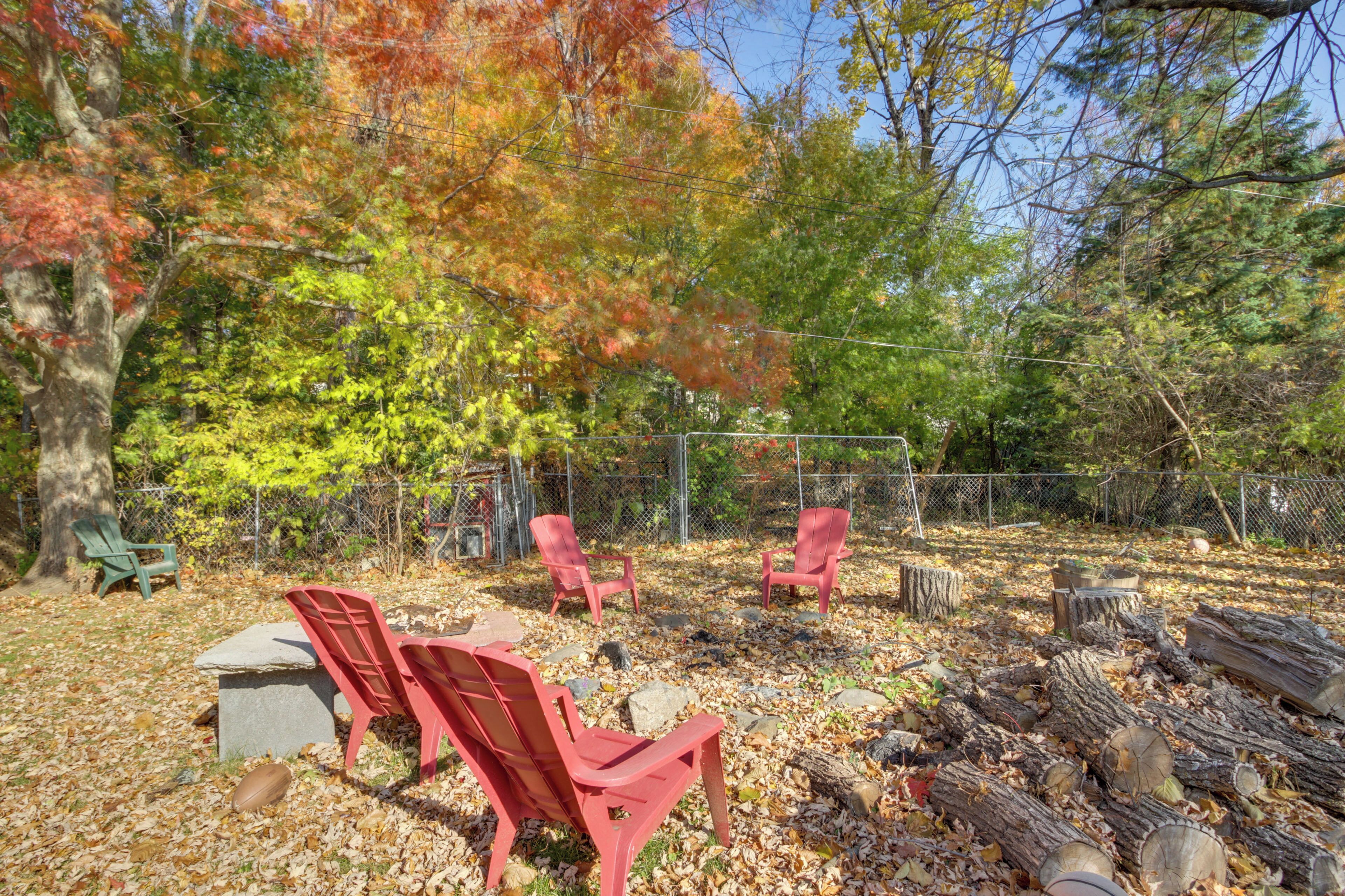 A fenced outdoor area with red chairs, a stone bench, and a pile of logs.