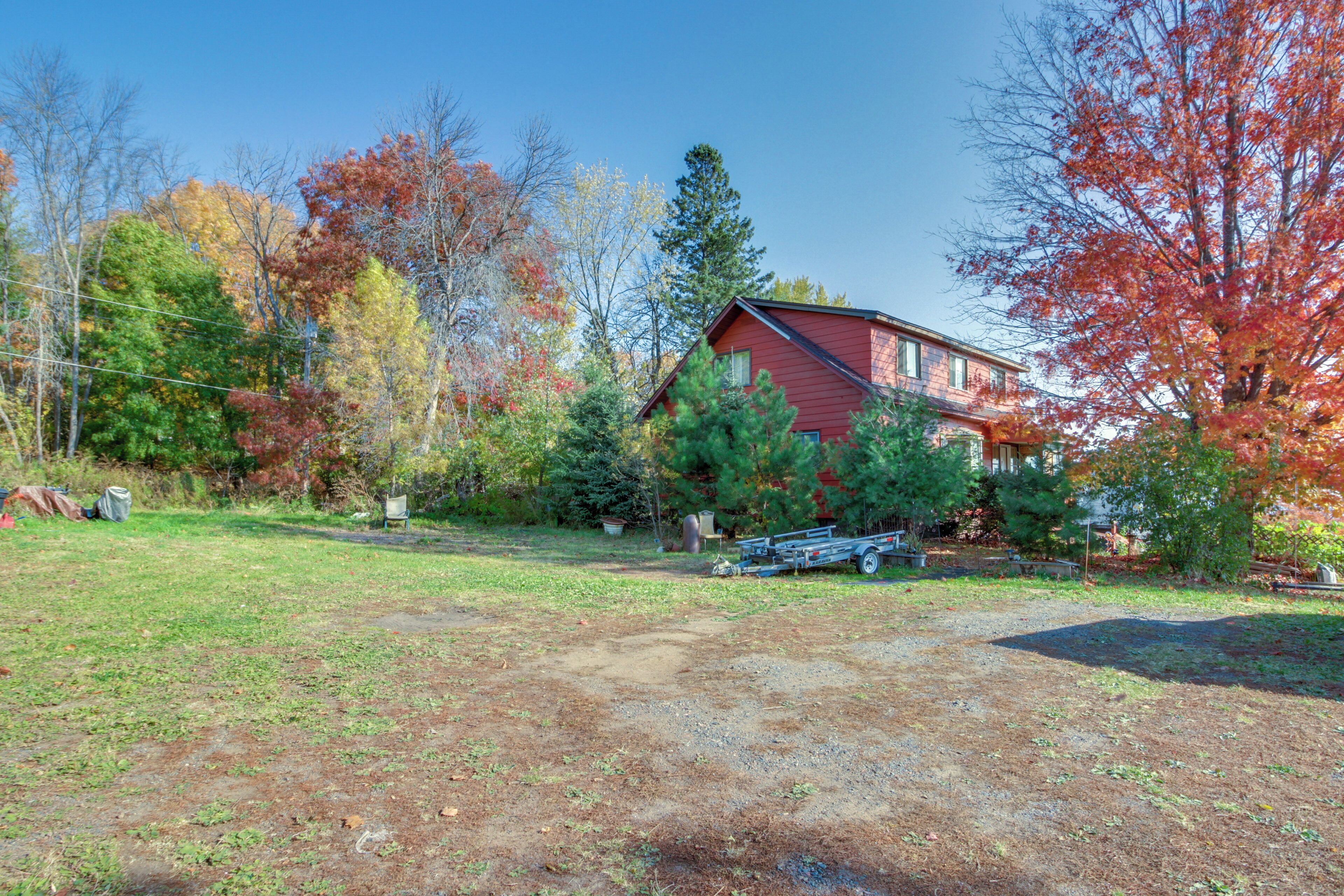 A red house with a gravel driveway, surrounded by trees with autumn foliage.