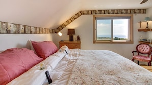 A bedroom with a large bed, a nightstand with a lamp, a window with a view, and a ceiling fan. - Spacious Duluth Home ~ 4 Mi to Lake Superior! (Duluth)