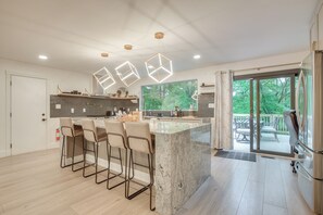 Eine moderne Küche mit Kochinsel, Barhocker, Pendelleuchten und Blick ins Freie.