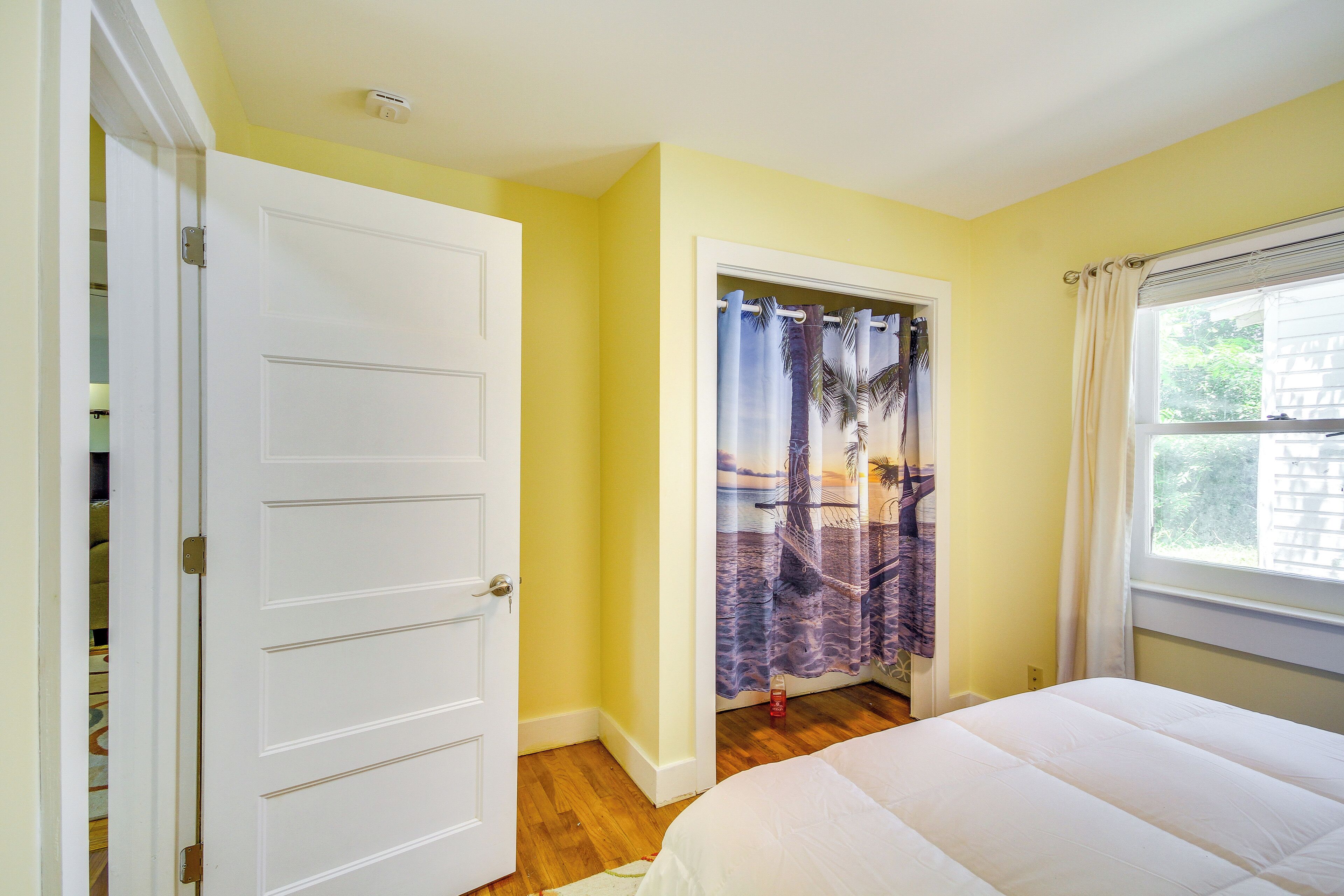 A bedroom with a bed, a door, a window with curtains, and a door leading to another room.