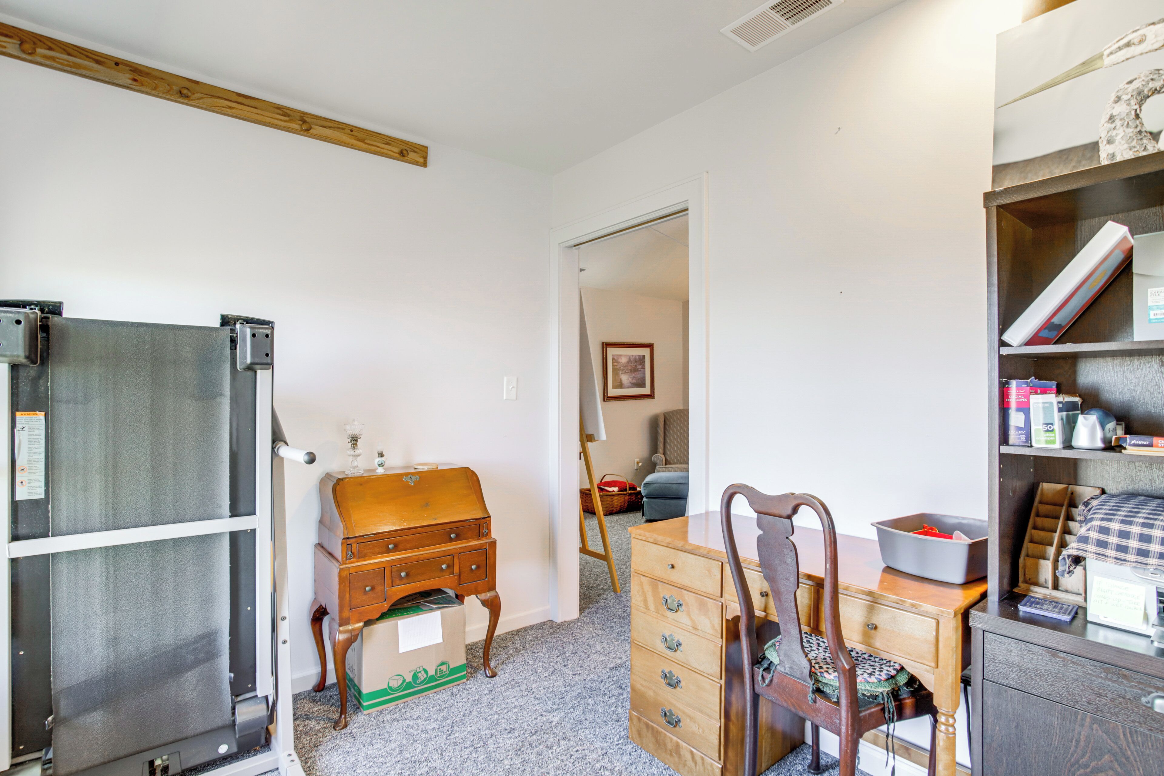 A compact room with a wooden dresser, a desk with a chair, a bookshelf, and a refrigerator.