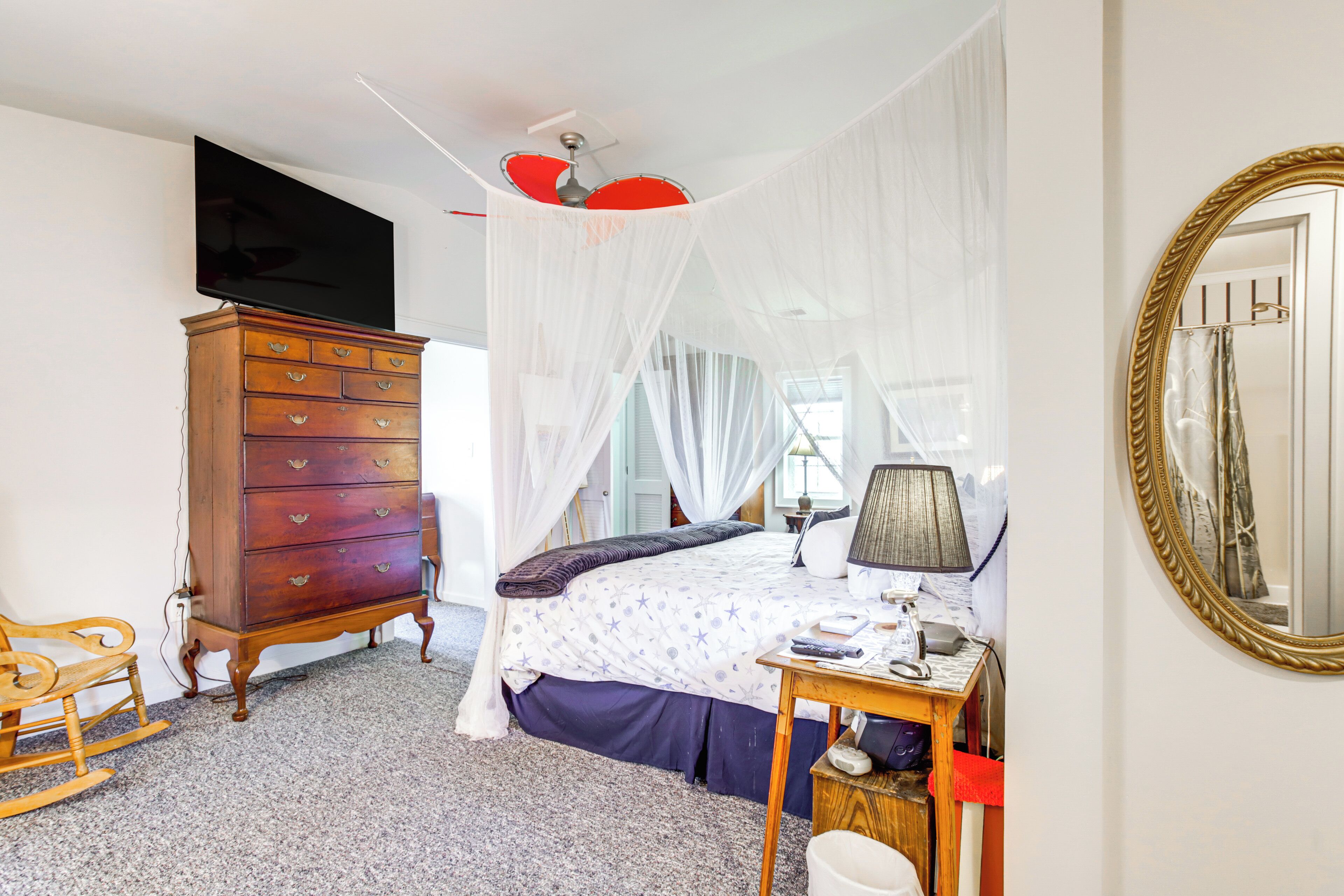 Een slaapkamer met een bed, een dressoir, een televisie, een spiegel en een plafondventilator.
