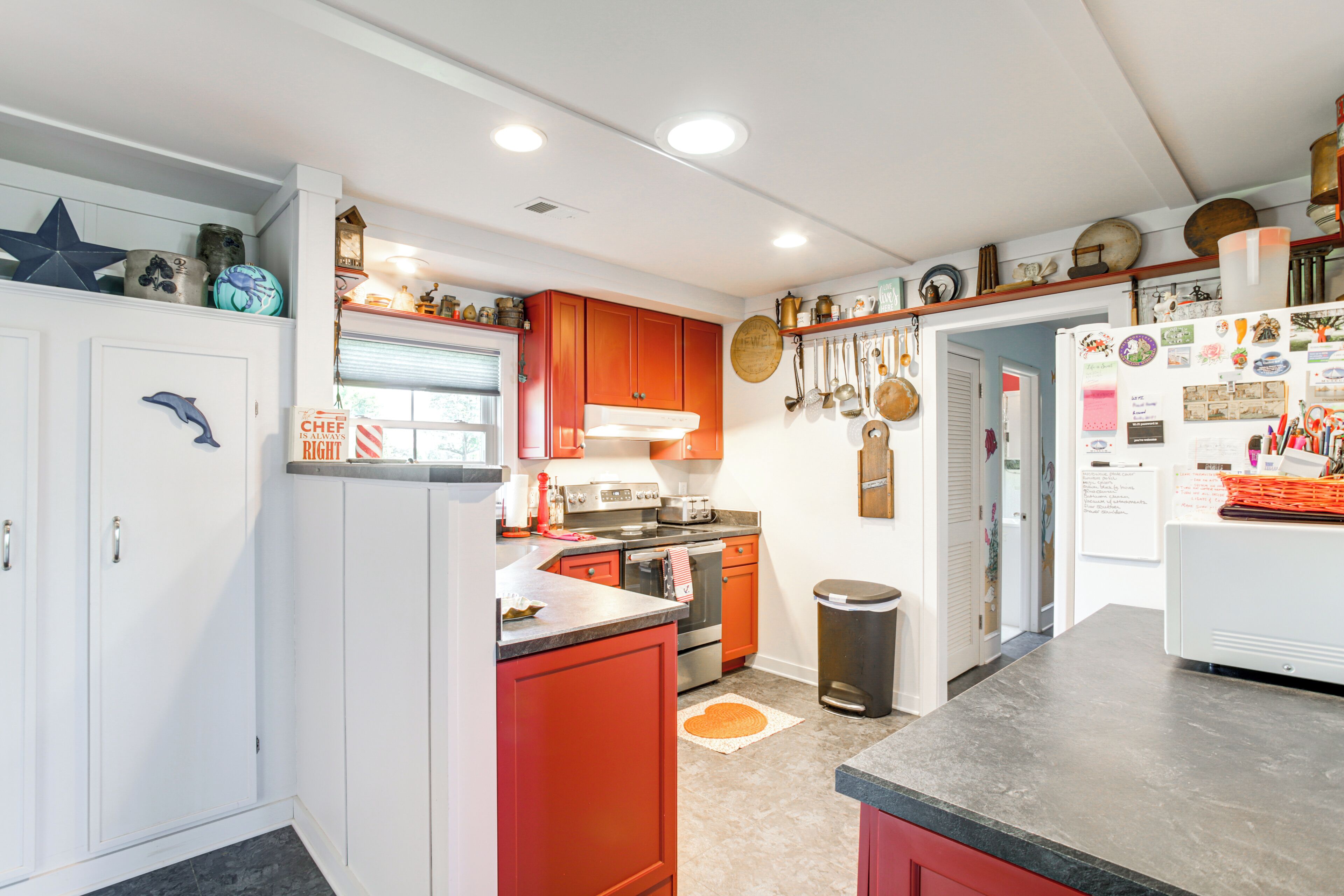 A kitchen with white and red cabinets, stainless steel appliances, and various kitchen utensils on the walls.