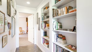 Een gang met een boekenplank vol boeken en ingelijste foto's aan de wanden.