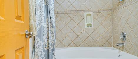 Un baño con bañera, cortina de ducha y toallero con artículos de aseo.