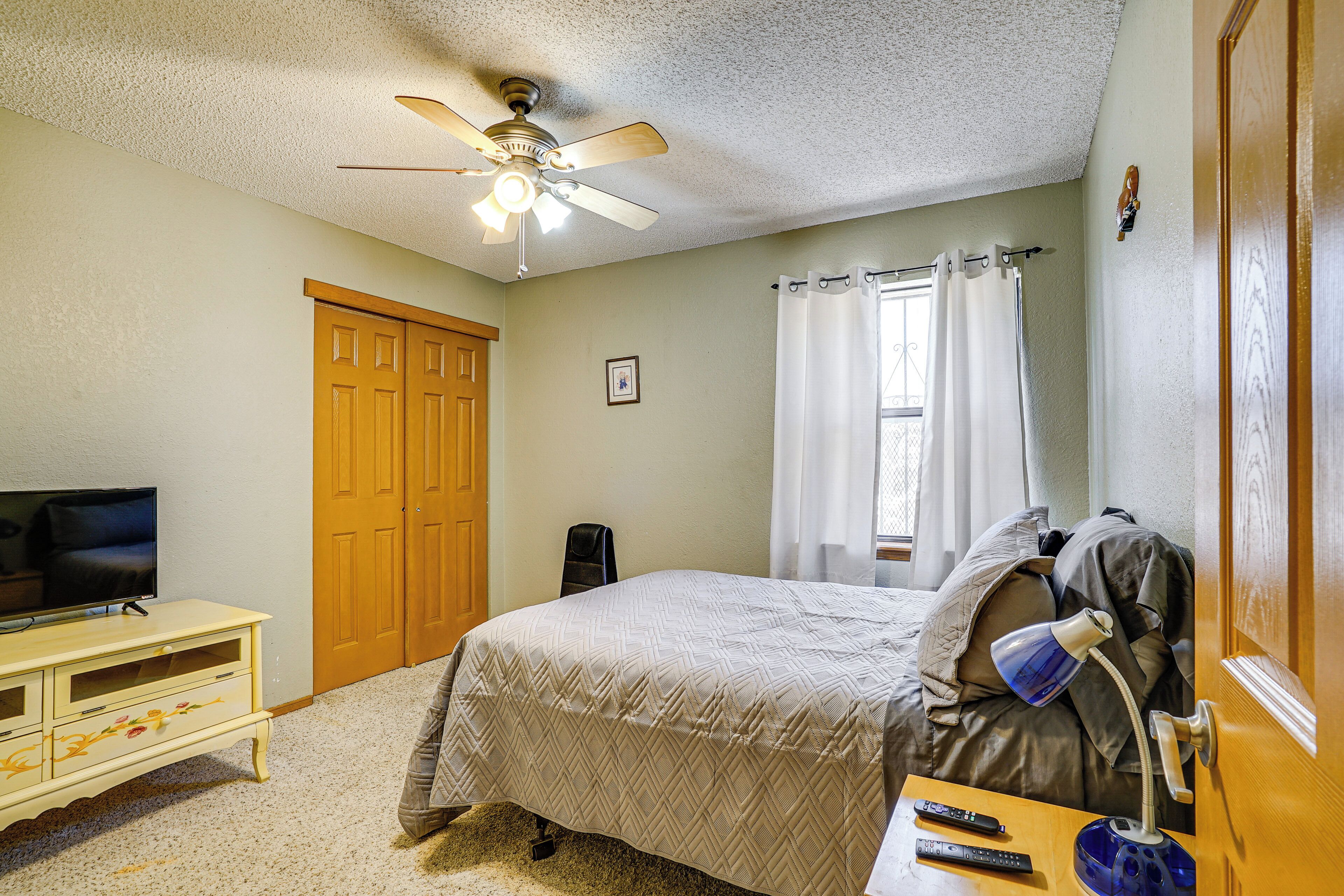 A bedroom with a bed, a ceiling fan, a TV on a dresser, and a window with curtains.