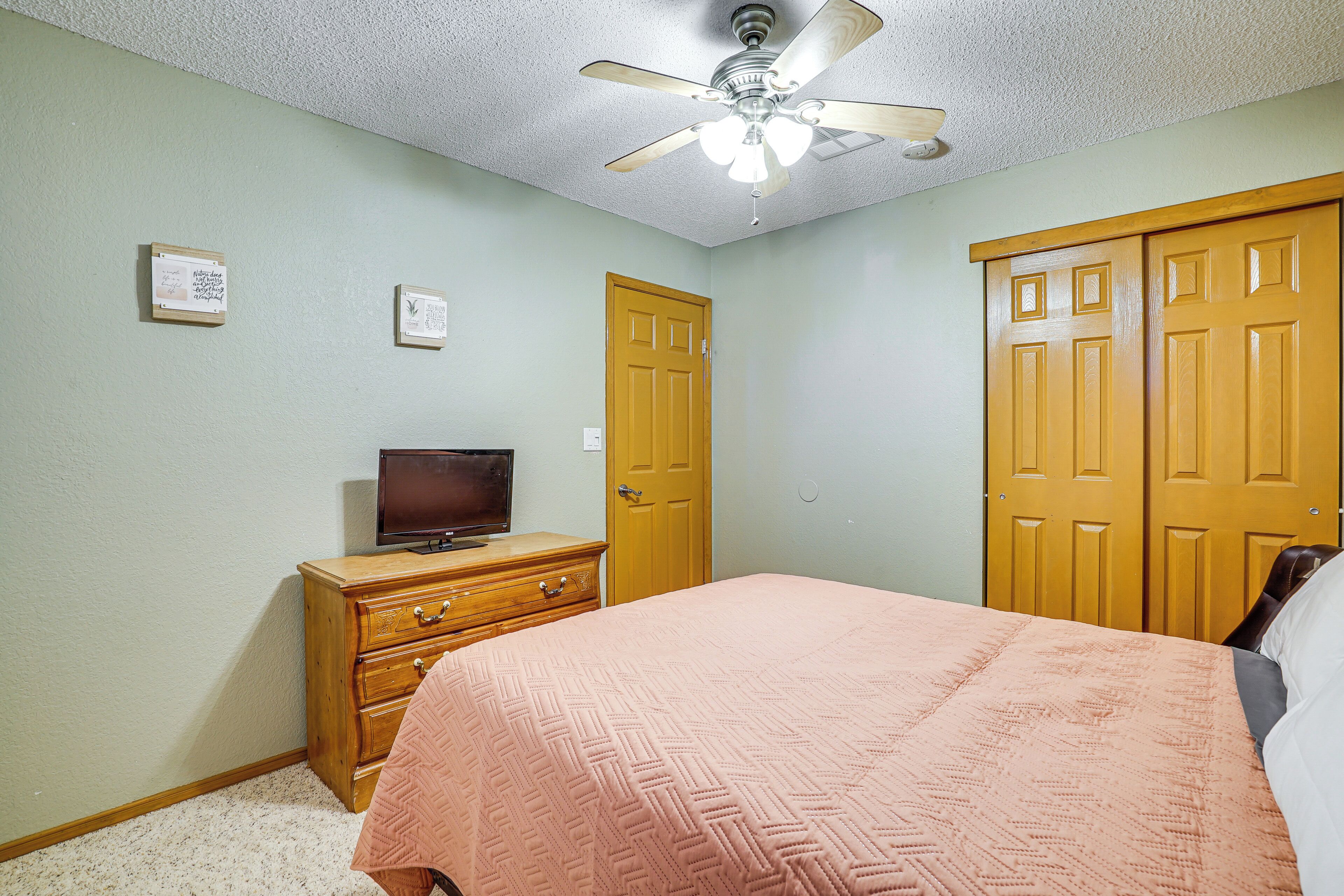 A bedroom with a bed, a dresser, a television on top, and a ceiling fan.