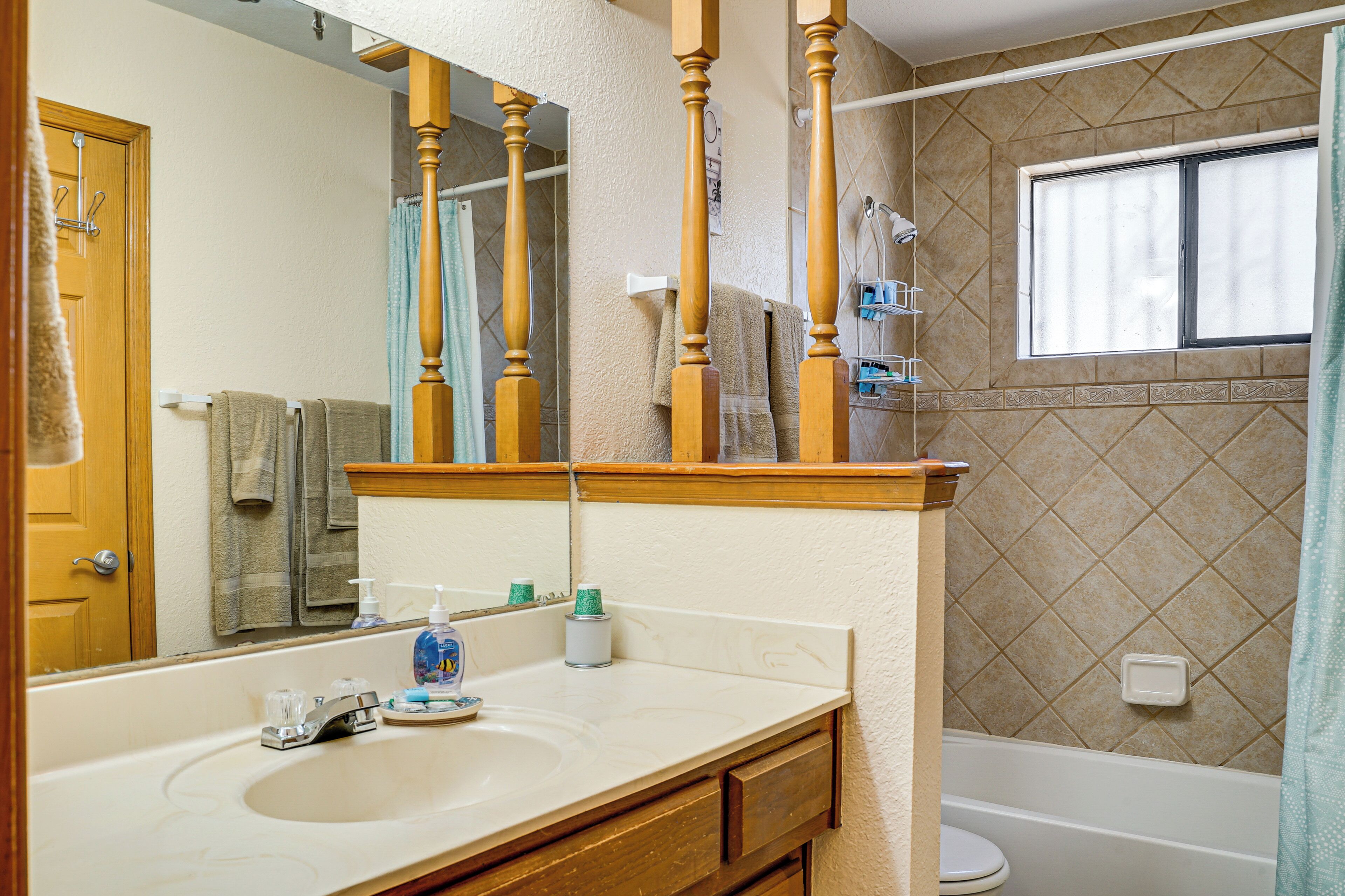 Une salle de bain avec un meuble-lavabo en bois, un grand miroir, une baignoire et une fenêtre.