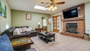 A living room with a fireplace, leather sofa, and a television mounted above it. - Pet-friendly El Paso Home ~ 9 Mi to Fort Bliss! (El Paso)