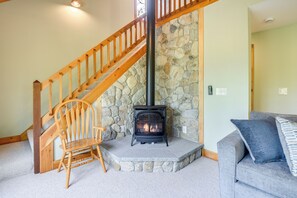 A cozy living room with a stone fireplace, a wooden staircase, and a gray sofa.