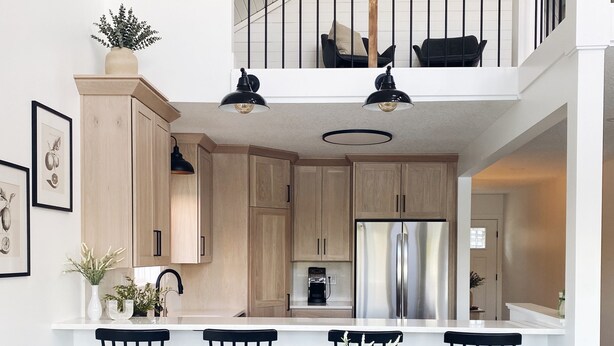 A modern kitchen with wooden cabinets, a stainless steel refrigerator, and a dining area with black chairs and a central plant. - [New!] Luxurious Lake Front Getaway!  (Wawaka)