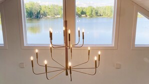 A room with a large chandelier, multiple windows, and a view of a lake. - [New!] Luxurious Lake Front Getaway!  (Wawaka)