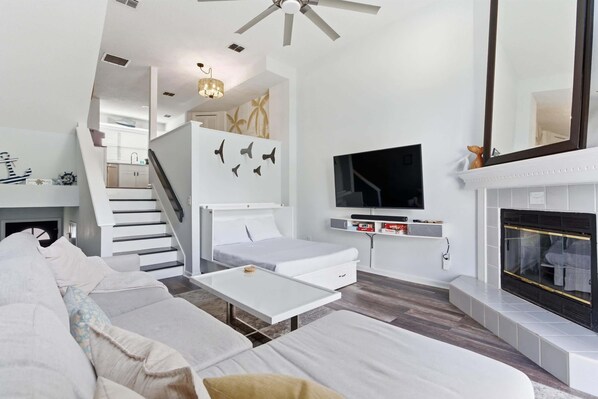 A modern living room with a sofa, a TV, a fireplace, and a staircase leading to an upper level. - 1 Block to Beach: Palm Paradise, A Coastal Oasis (Jacksonville Beach)