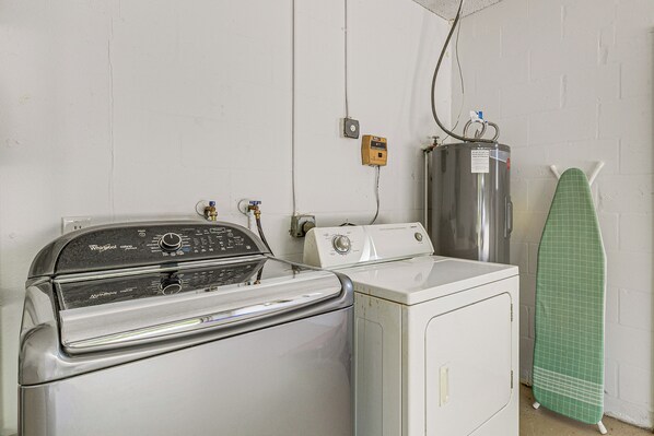 A laundry area with a front-loading washer, a stacked washer and dryer, and a green ironing board against a white brick wall. - Heated Pool & Dog-friendly Yard! Spring Hill Home (Spring Hill)