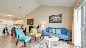 A modern living room with a blue sofa, a red ottoman, and a dining area with a table and chairs. - Charming Condo w/ Balcony, 1 Mi to UNC Charlotte! (Charlotte)