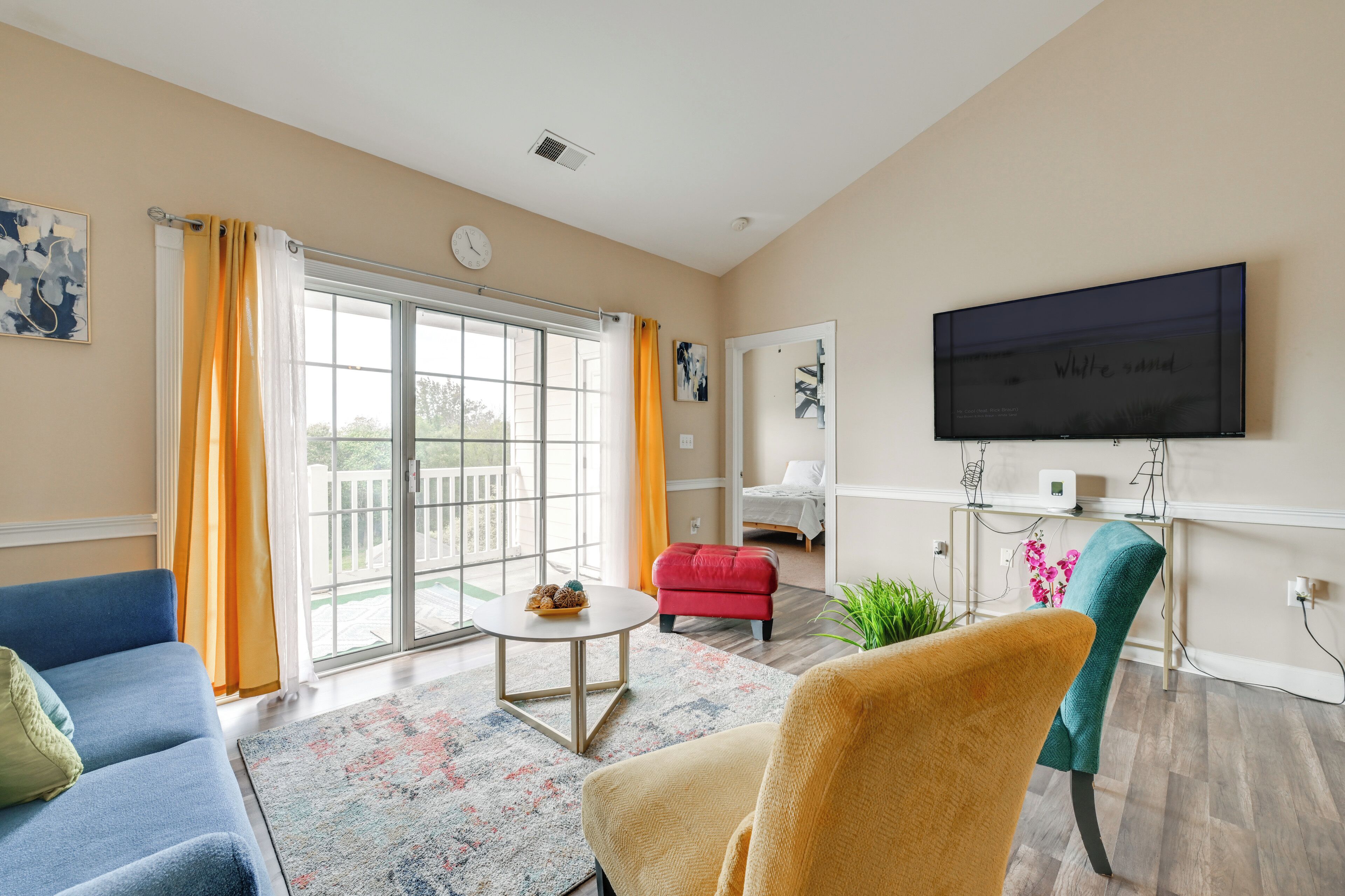 Un salon comprenant un canapé, un fauteuil, un pouf et un téléviseur à écran plat fixé au mur.