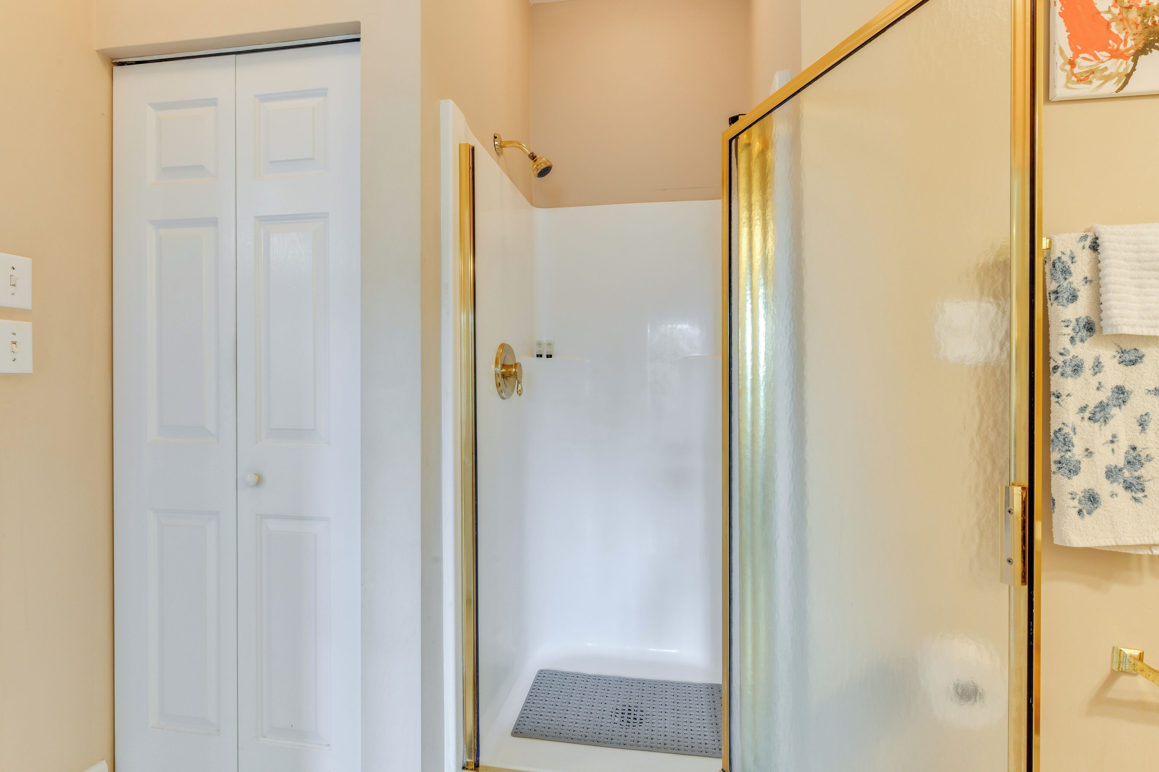 A bathroom with a white door, a shower with a glass door, and a towel rack with a floral towel.