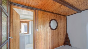 Una habitación con paredes de madera, piso blanco, un espejo redondo y una escalera de madera.