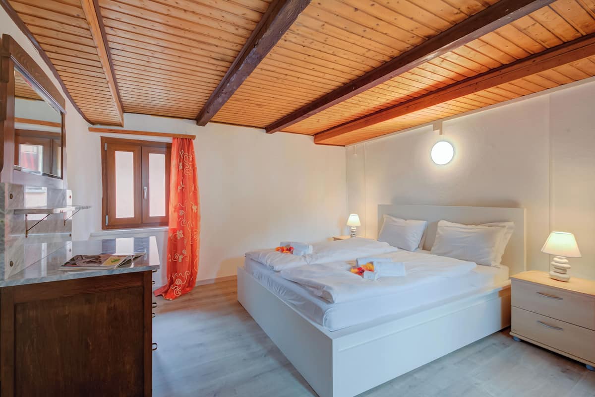 Ein Schlafzimmer mit Holzboden, einem Bett mit weißer Bettwäsche, einem Nachttisch mit Lampe und einer Holzkommode.