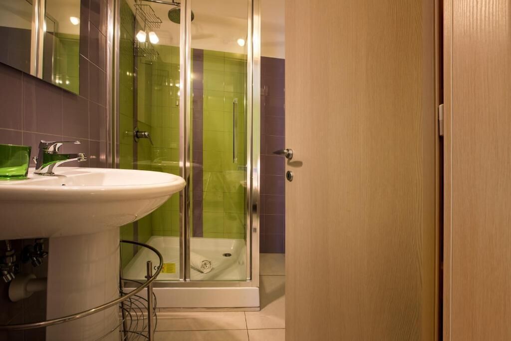 Een badkamer met een glazen douchecabine, een witte wastafel en een houten deur.